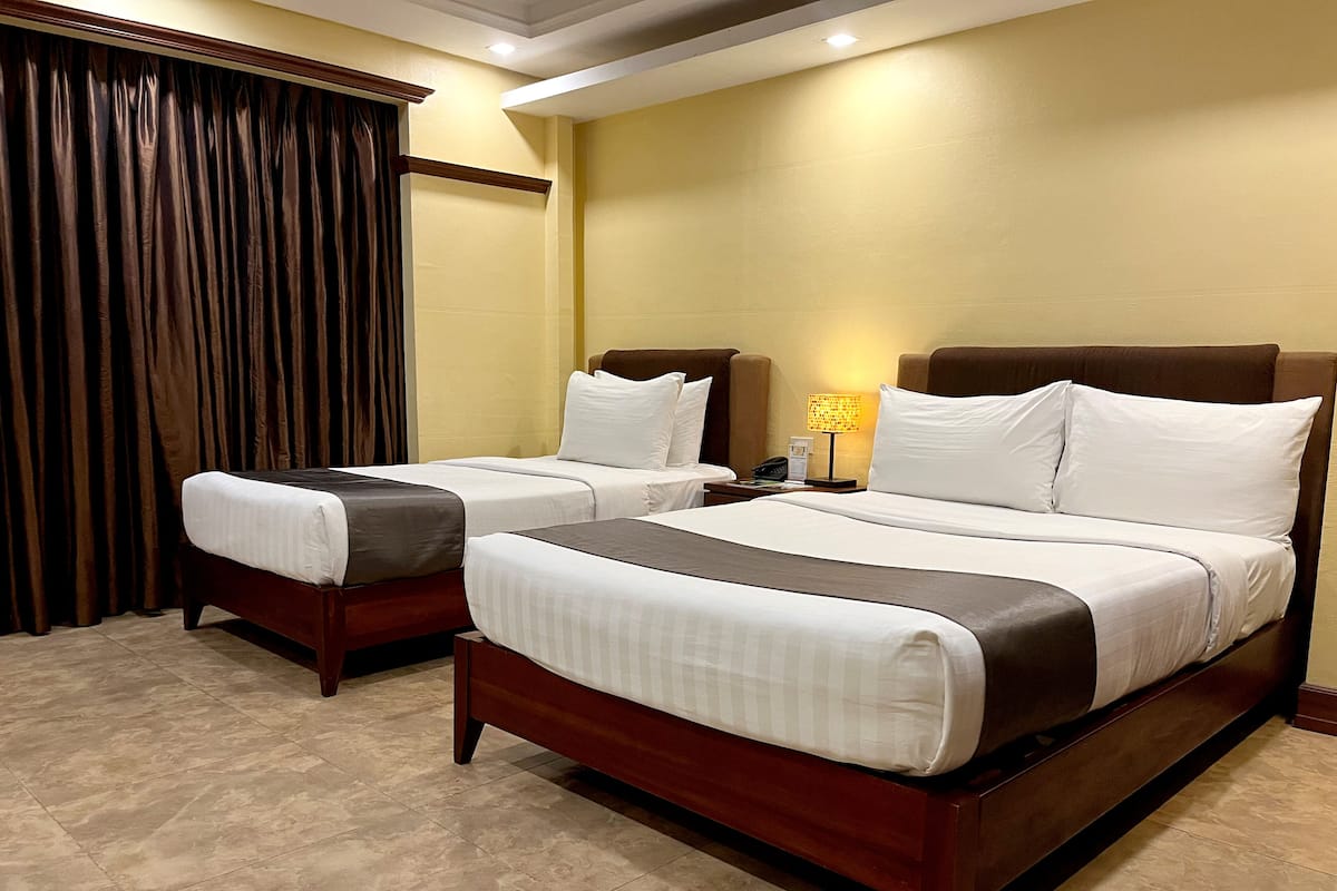 A hotel room with two beds, a nightstand, a lamp, and a window with curtains.