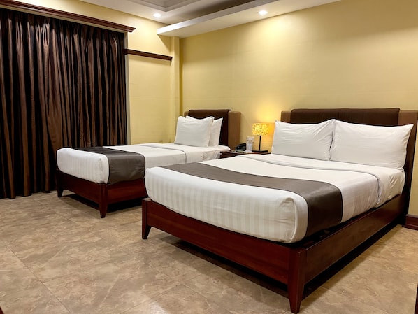 Habitación de hotel con dos camas, una mesita de noche, una lámpara y una ventana con cortinas.