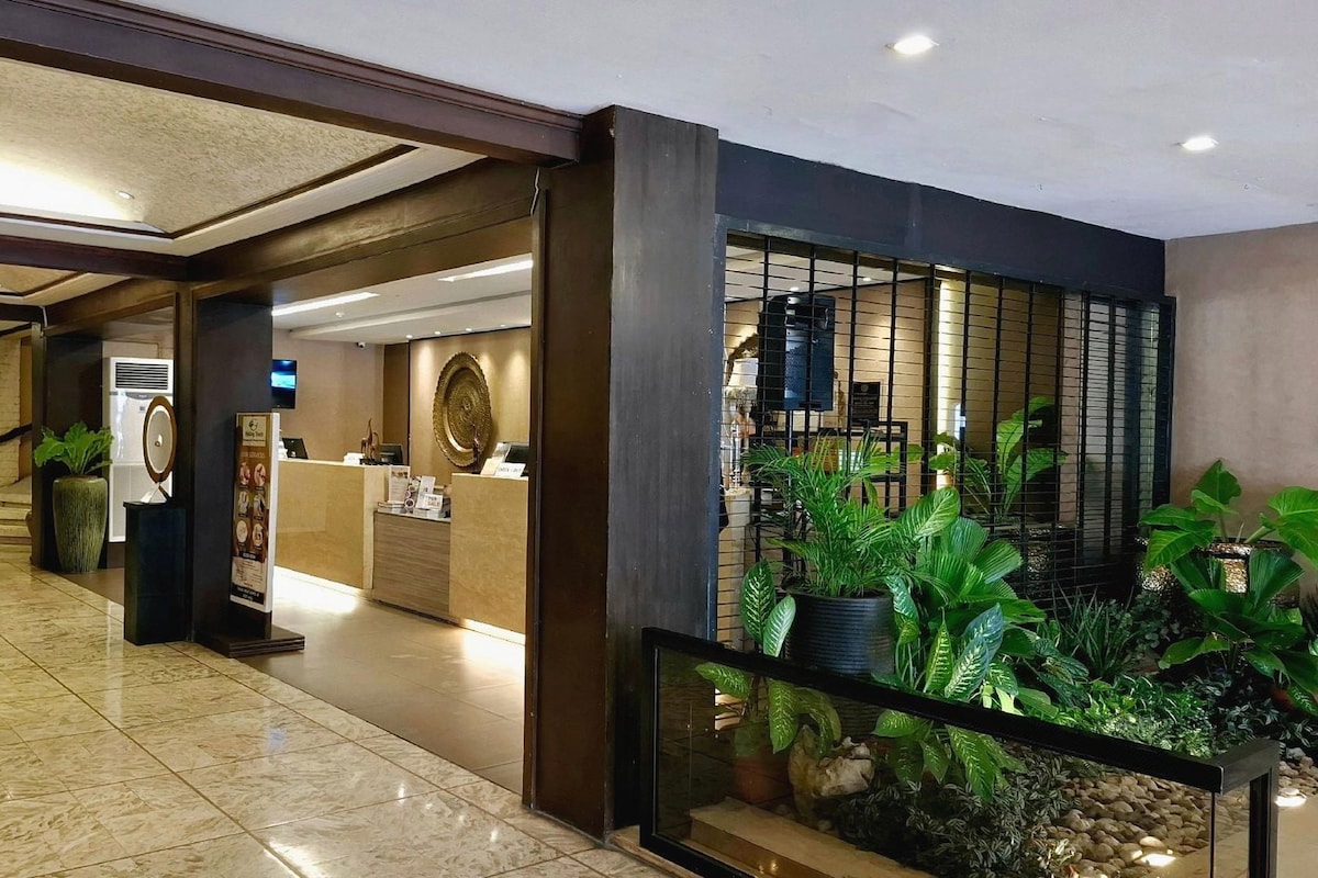 Un vestíbulo de hotel con mostrador de recepción, una escalera y una zona con plantas en macetas.