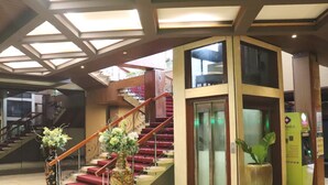 A hotel lobby with a staircase, a reception desk, and a large vase with flowers. - Hotel Del Rio (Iloilo)