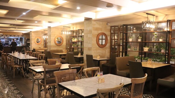 A restaurant with multiple tables and chairs, a bar area, and shelves with plants. - Hotel Del Rio (Iloilo)
