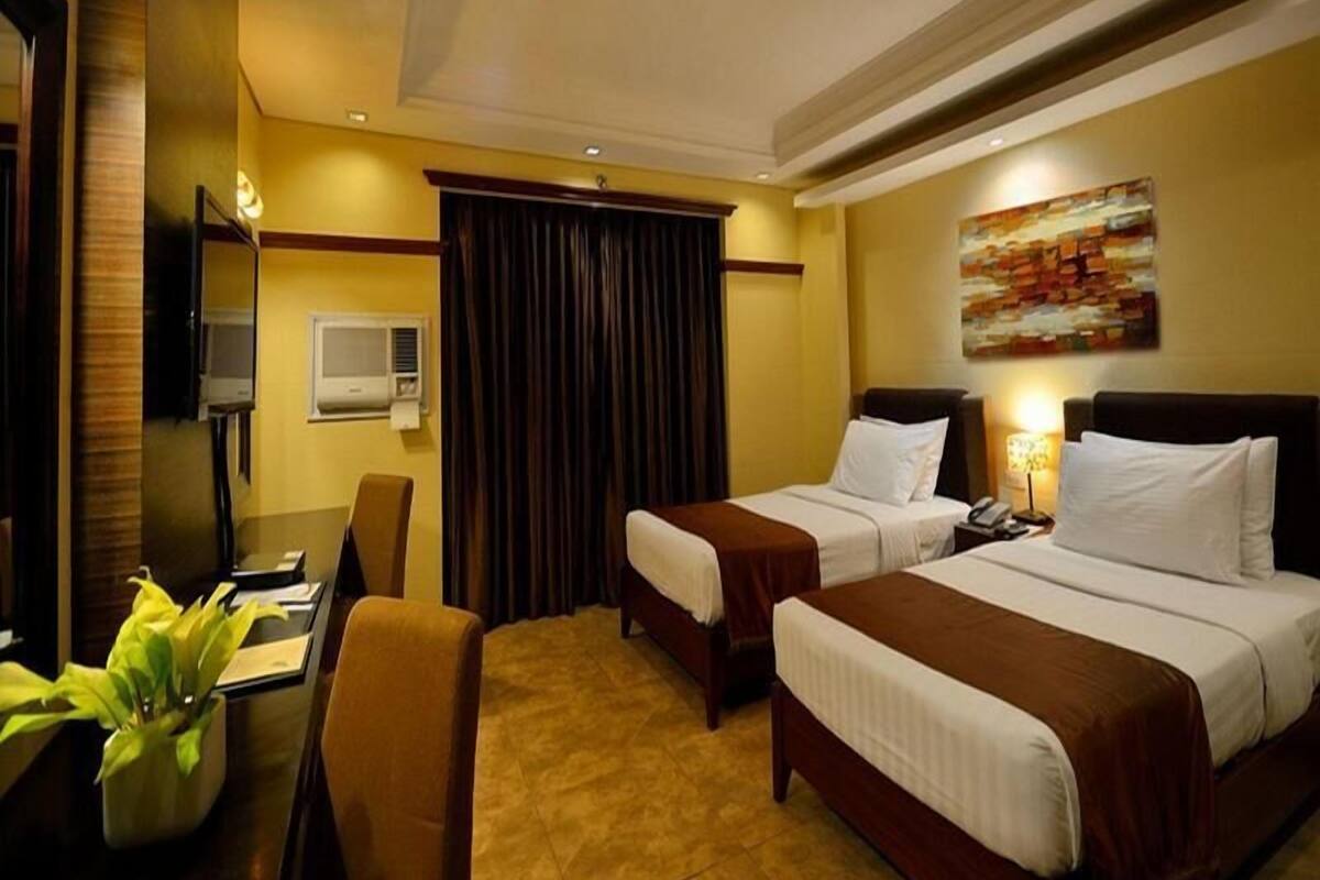 A hotel room with two beds, a desk, a chair, a TV, and an air conditioning unit.