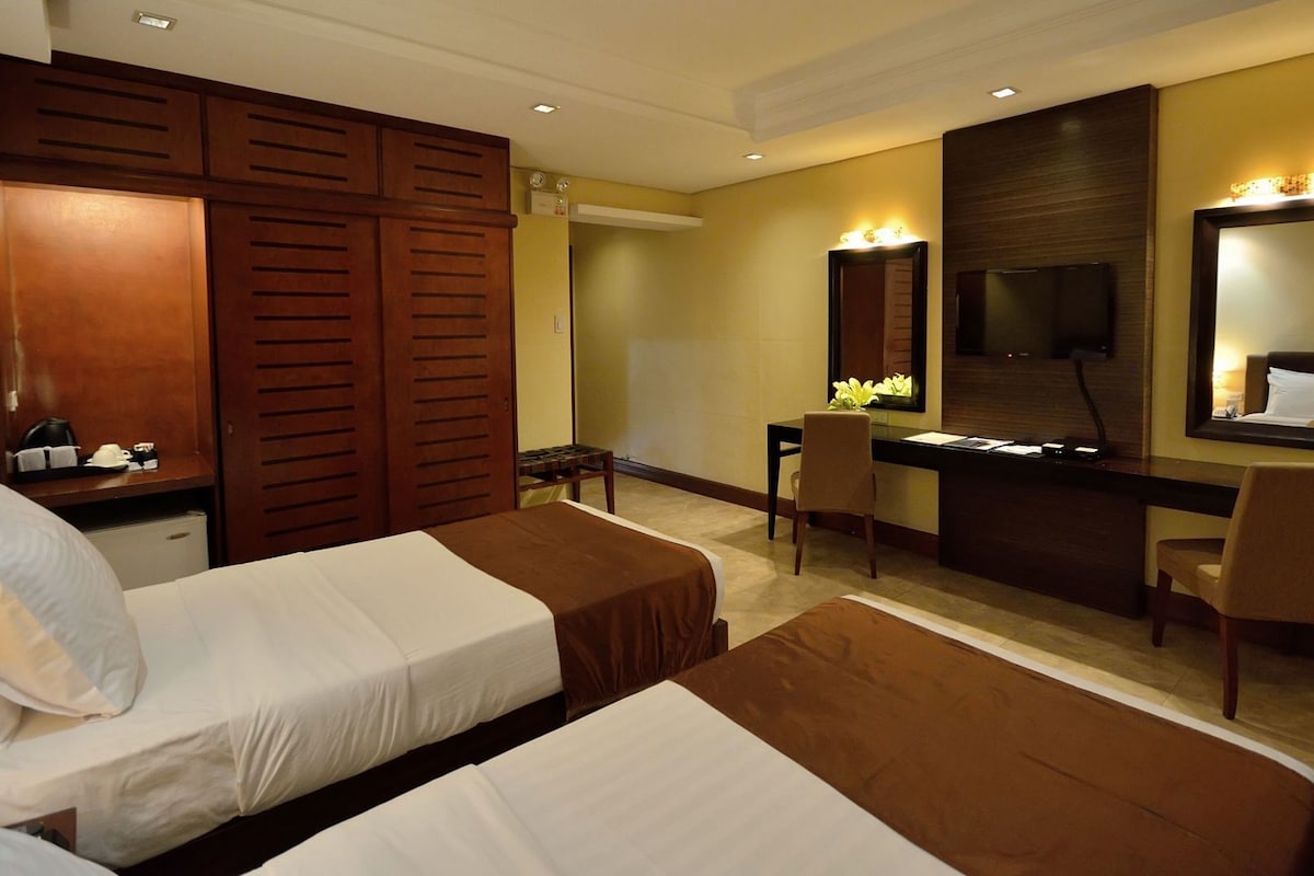 Habitación de hotel con dos camas, un escritorio, una silla, un televisor y un espejo grande.