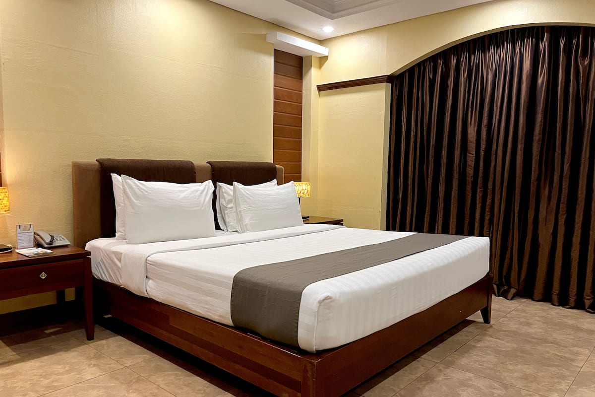 A hotel room with a large bed, a nightstand, a lamp, and a curtain.