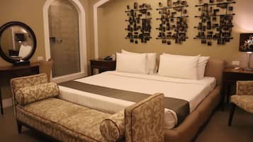 A hotel room with a large bed, a sofa, a desk, a mirror, and a wall-mounted artwork.