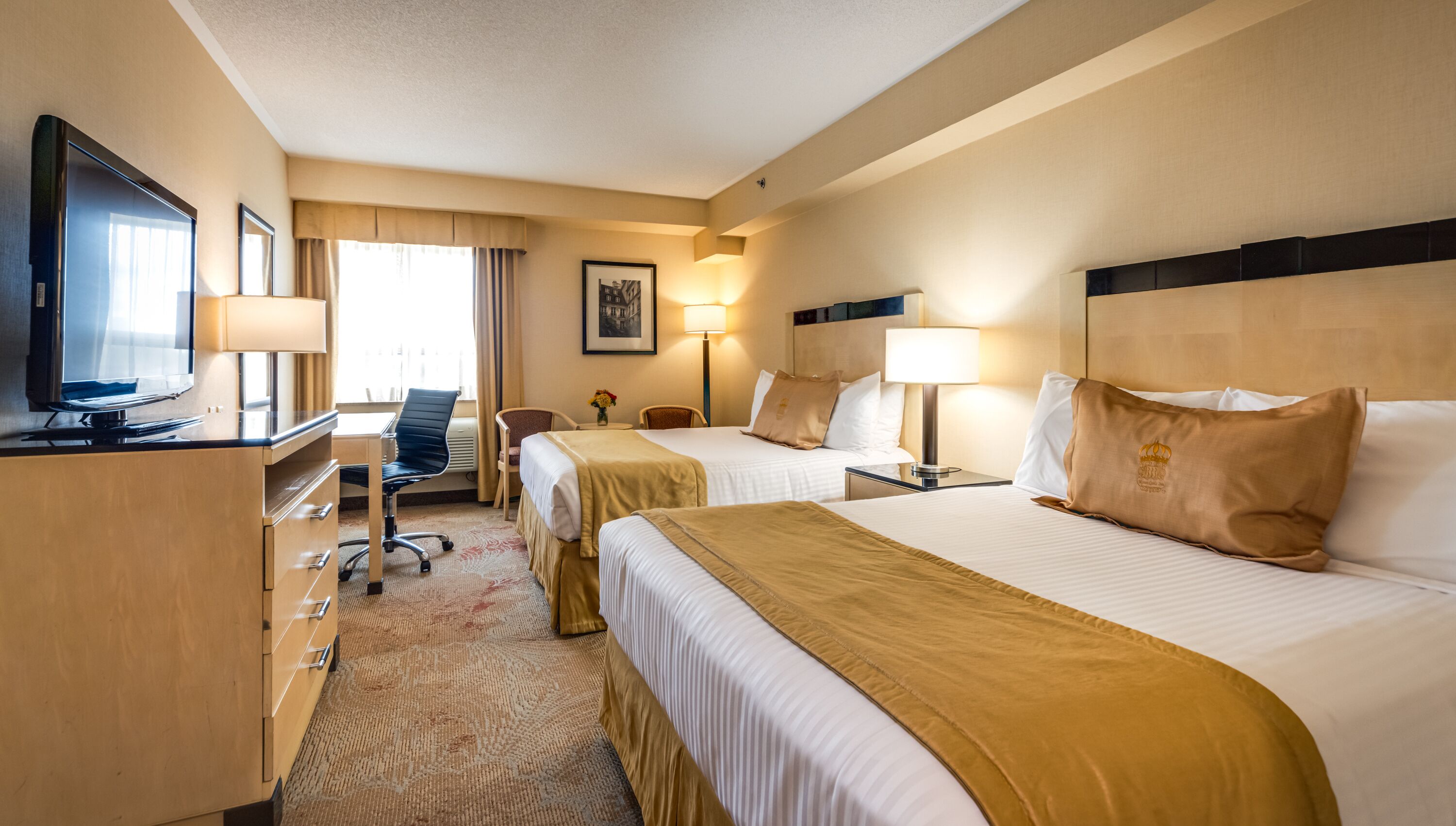Een hotelkamer met twee bedden, een bureau met een televisie, een stoel en een bureaulamp.