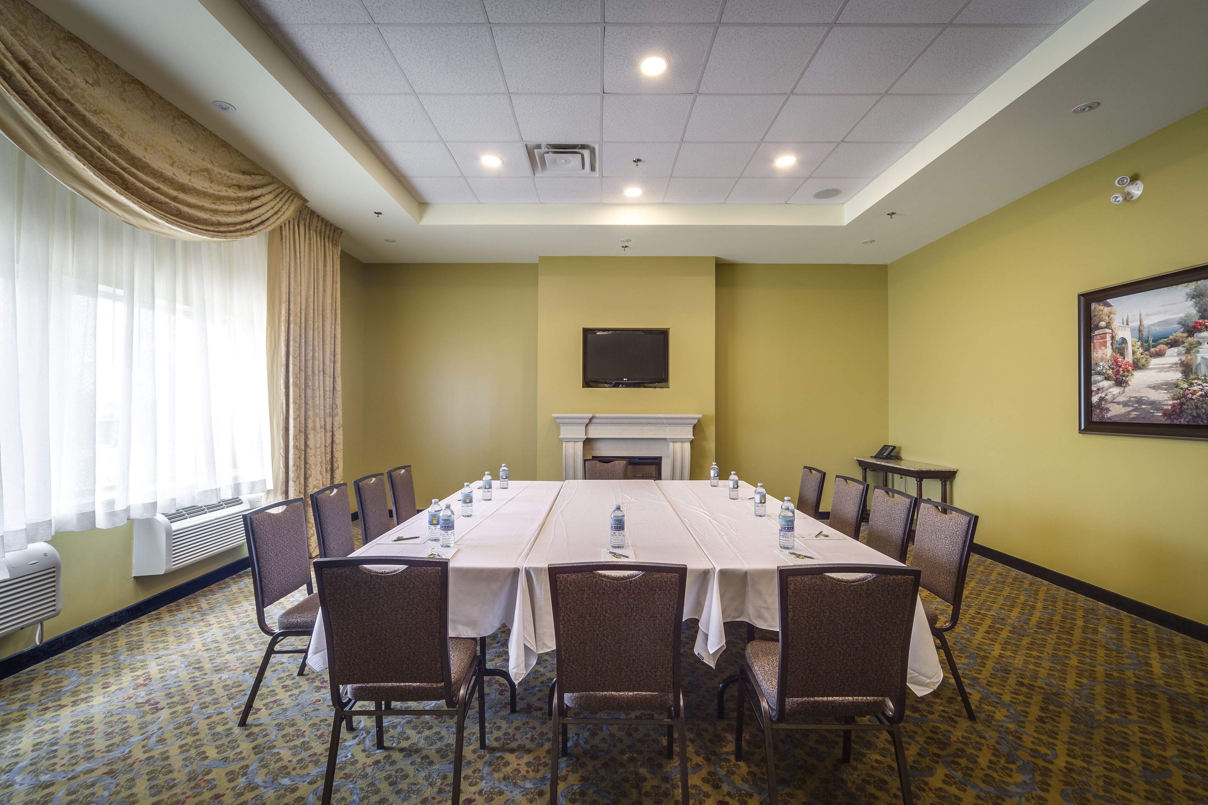 A conference room with a long table, chairs, a fireplace, and a television on the wall.