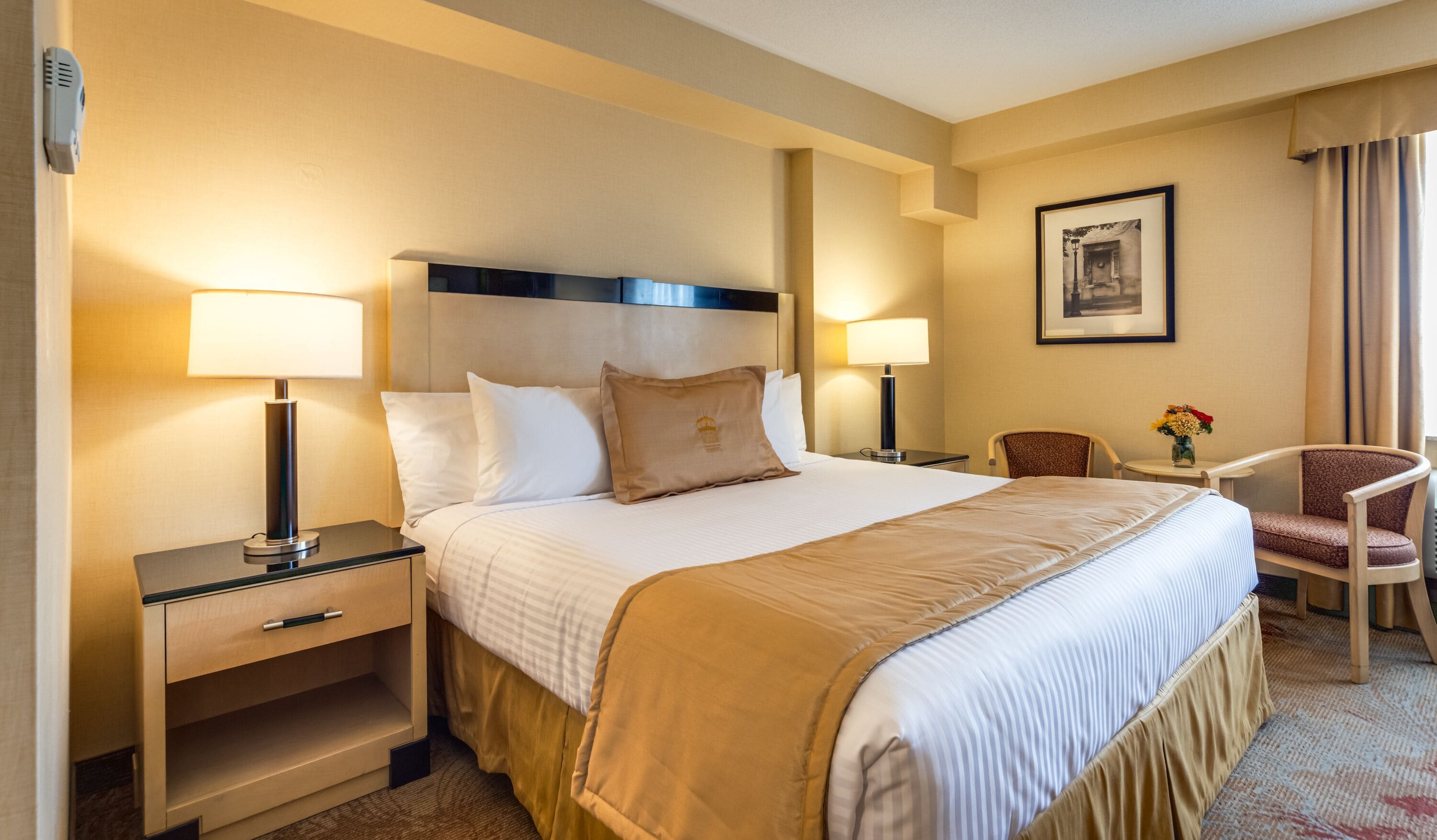 A hotel room with a large bed, two bedside tables, a chair, and a small table with a vase of flowers.
