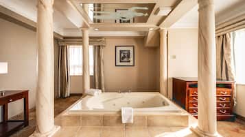 Ein geräumiges Badezimmer mit einer großen Badewanne, Marmorsäulen und einem Holzkabinent.