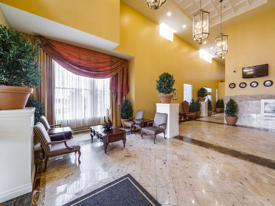 A spacious lobby with a marble floor, a large potted plant, a fireplace, and a television mounted on the wall.