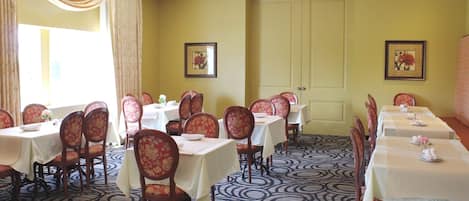 Un espace repas comprenant plusieurs tables et chaises, une moquette à motifs et deux tableaux encadrés accrochés aux murs.