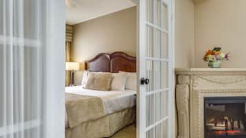 A hotel room with a bed, a fireplace, and a door leading to another room.