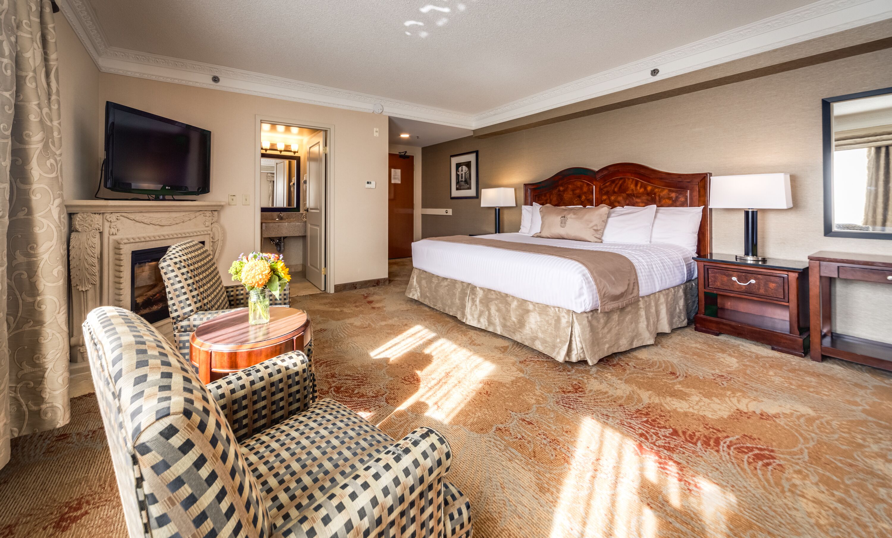 A hotel room with a large bed, a television, a fireplace, a sofa, and a small table with flowers.