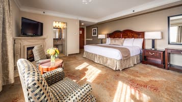 A hotel room with a large bed, a television, a fireplace, a sofa, and a small table with flowers.