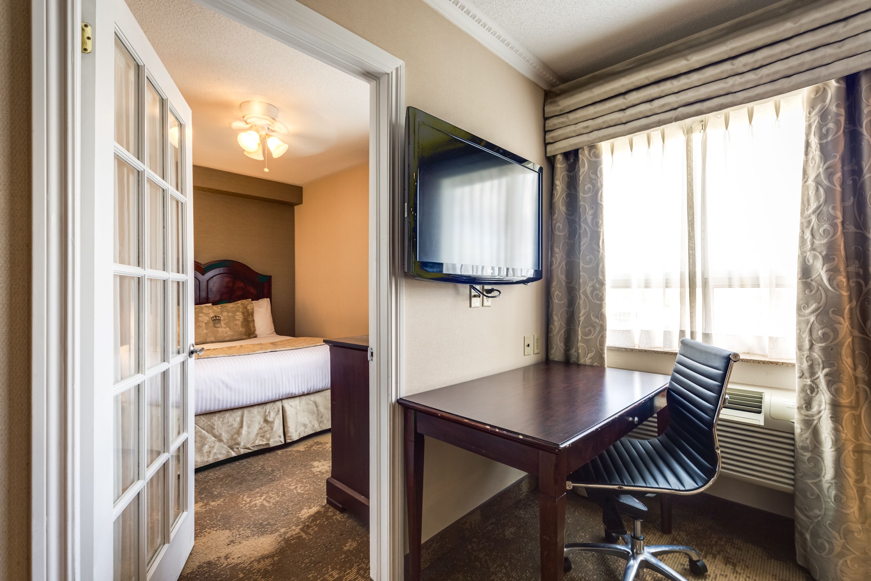 A hotel room with a bed, a desk, a chair, a television, and a window with curtains.