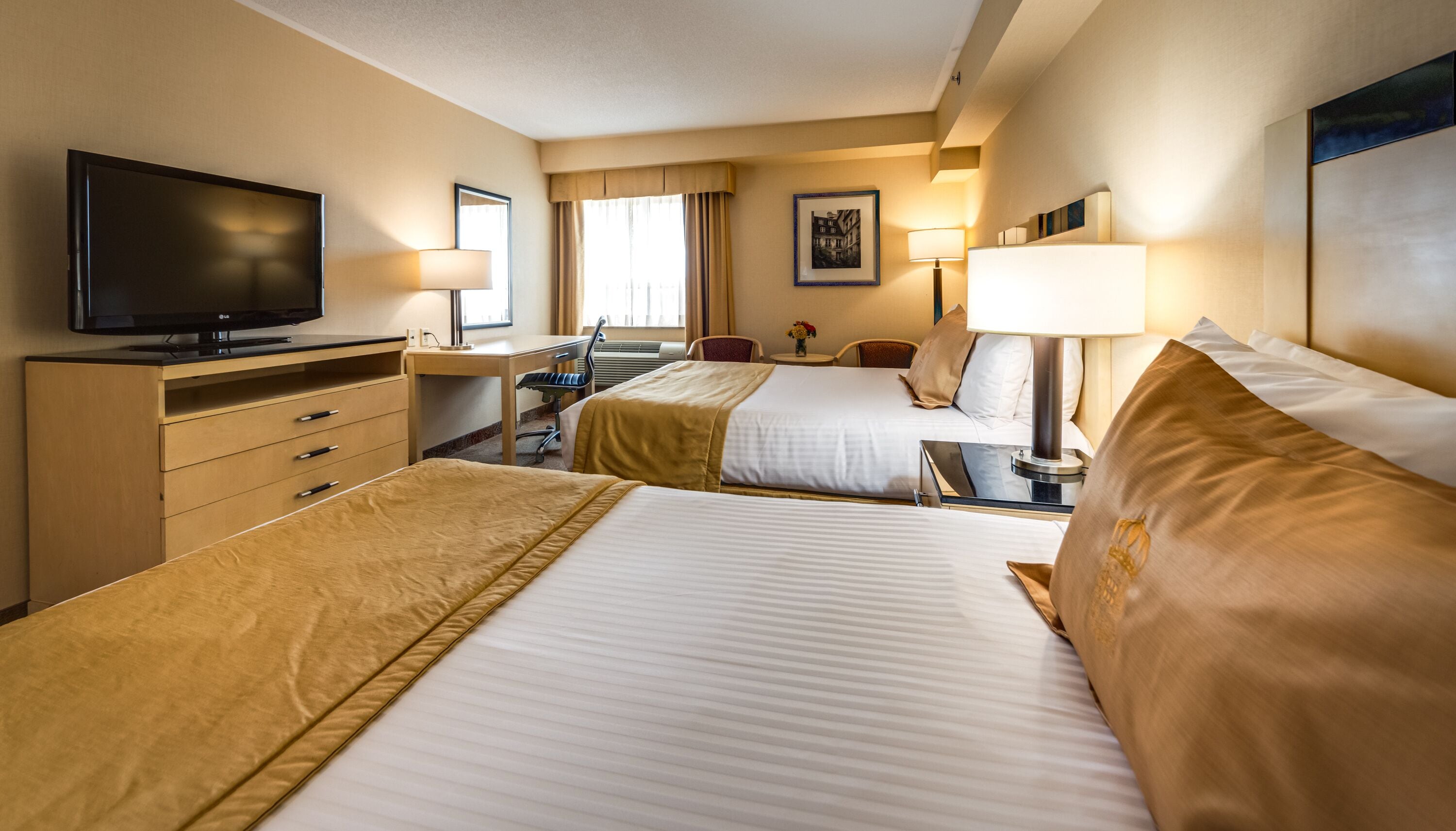 A hotel room with two beds, a desk, a chair, a TV, and a window with curtains.