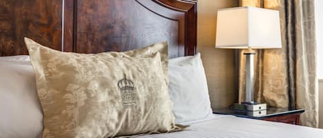 Una cama bien hecha con un cojín decorativo, una lámpara de noche y un cabecero de madera.