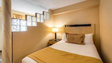 A hotel room with a bed, a nightstand, a lamp, and a window with a view of the city.