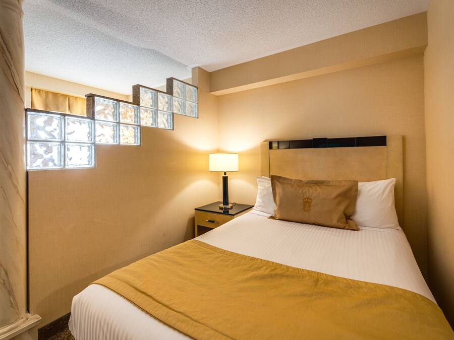 A hotel room with a bed, a nightstand, a lamp, and a window with a view of the city.