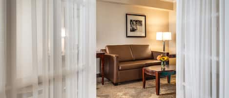 A hotel room with a brown leather sofa, a small wooden side table, a lamp, and a framed picture on the wall.