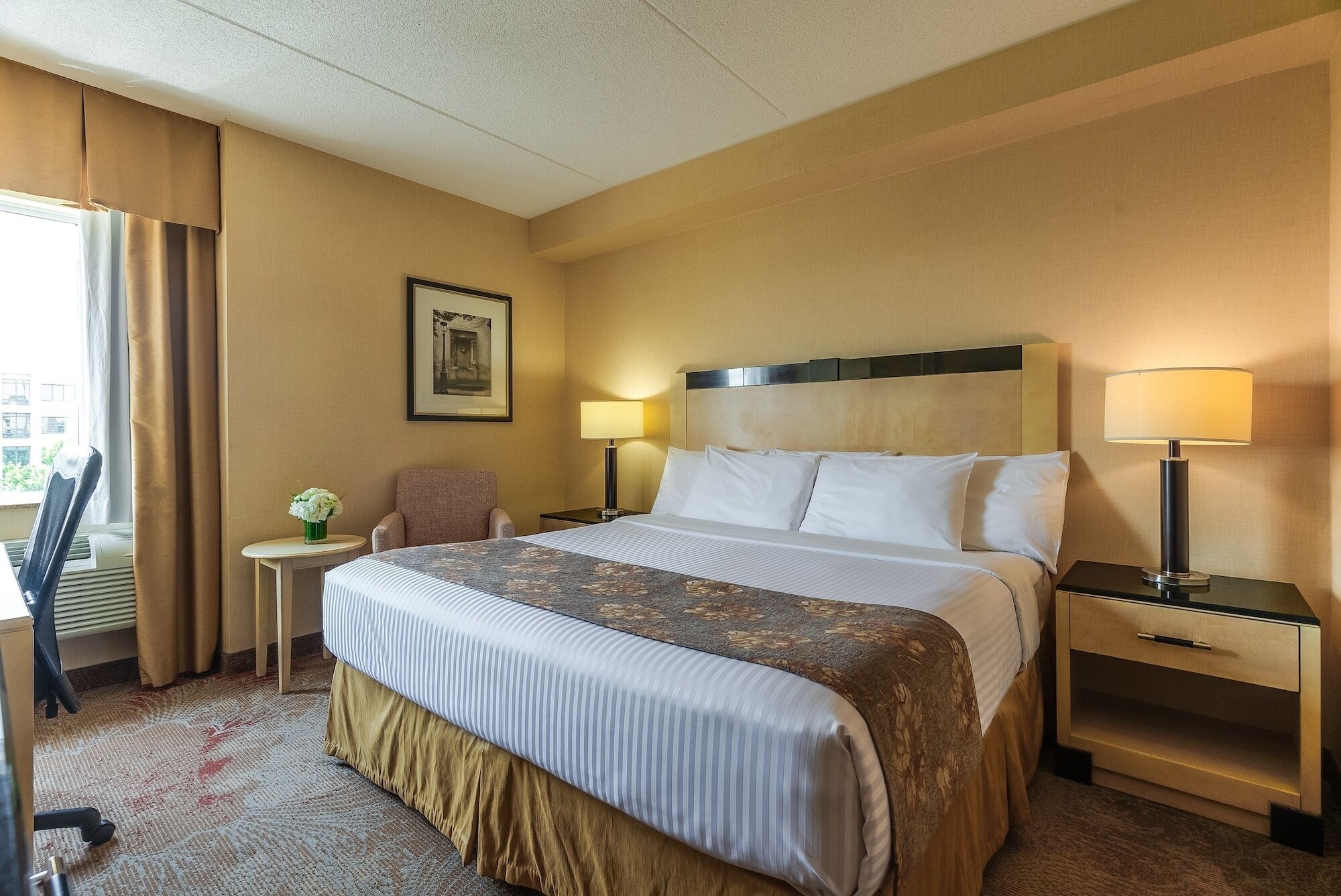 A hotel room with a bed, bedside tables, a chair, a lamp, and a framed picture on the wall.