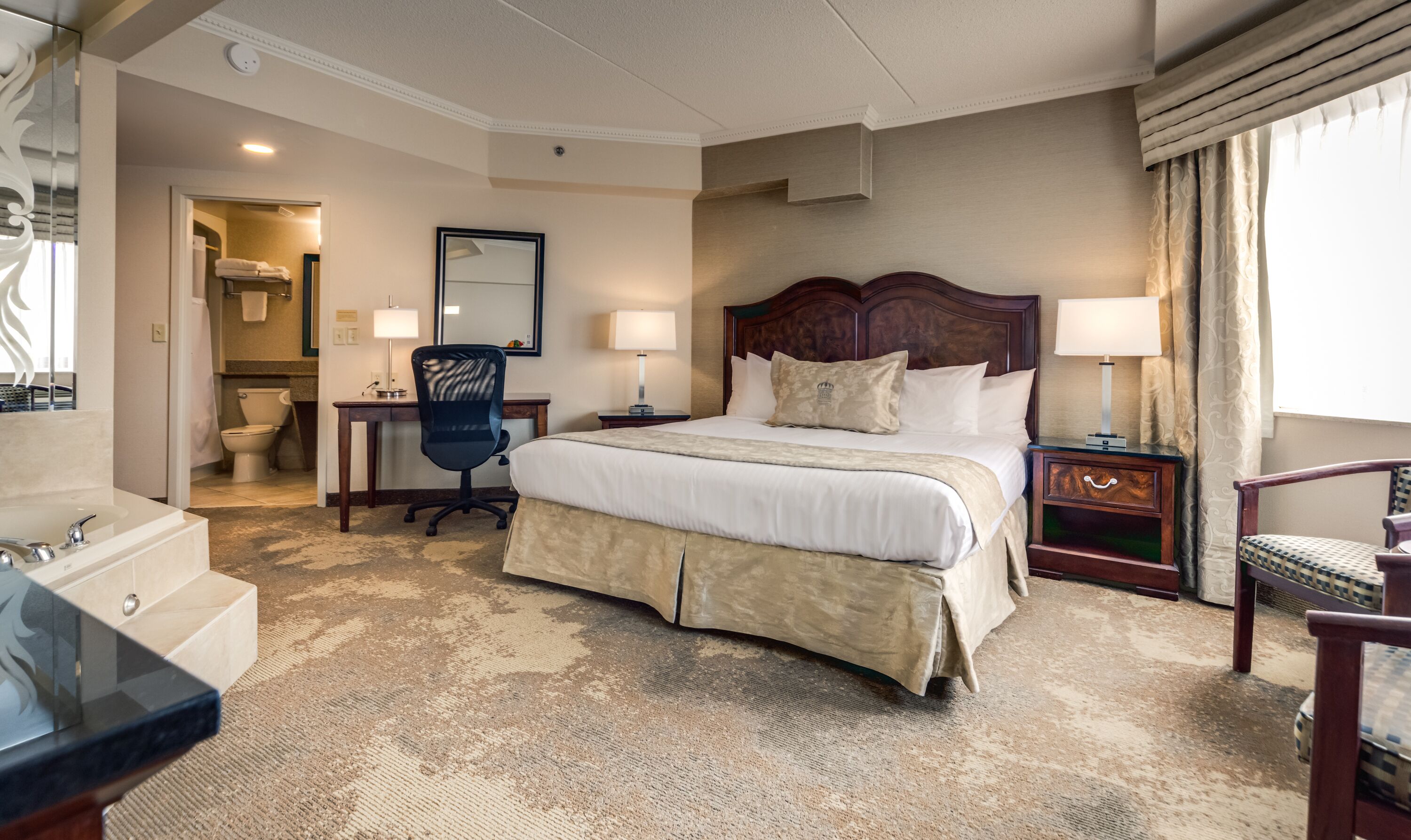 Habitación de hotel con una cama grande, un escritorio, una silla, baño y vistas al exterior.