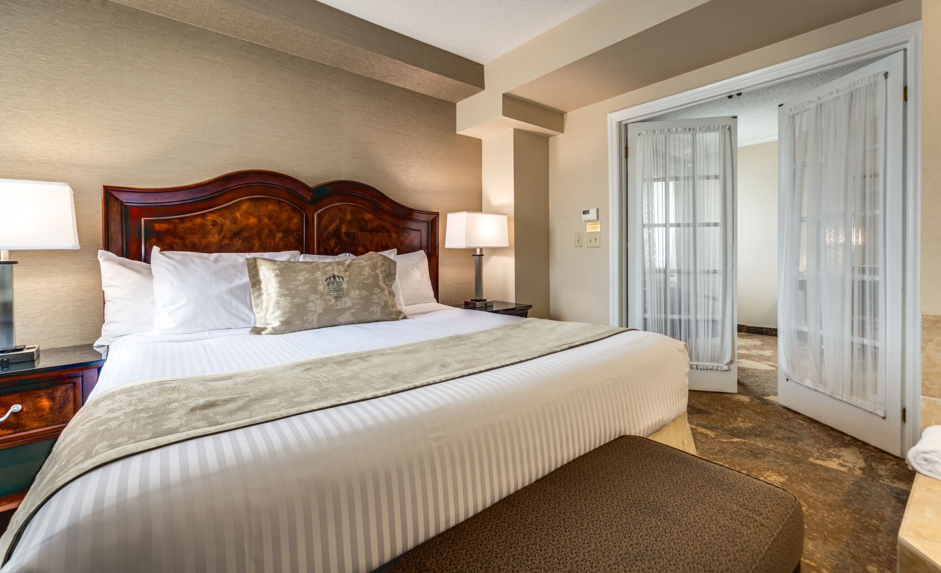 A hotel room with a large bed, a wooden headboard, a nightstand with a lamp, a robe, and a door leading to a bathroom.