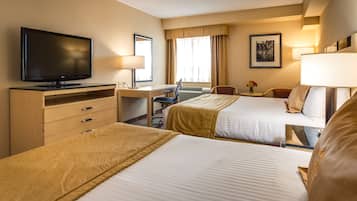 A hotel room with two beds, a desk with a chair, a television, and a window with curtains.
