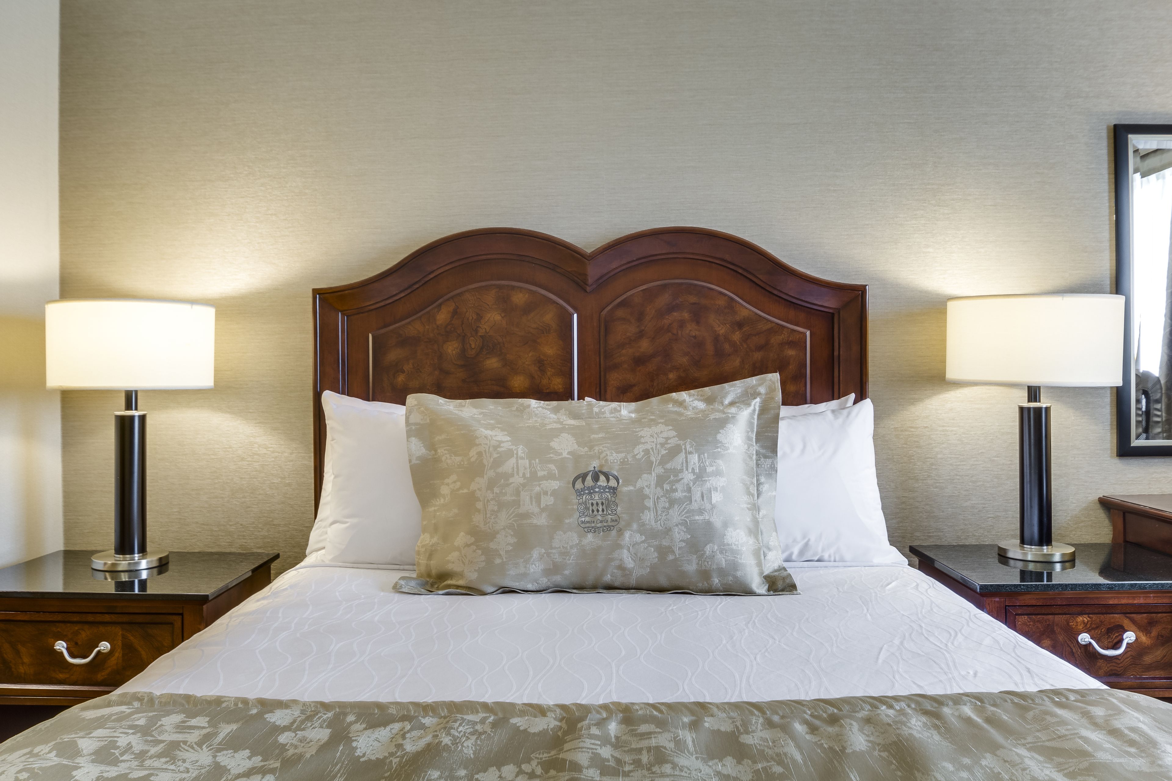 A neatly made bed with a decorative pillow, two bedside tables with lamps, and a wooden headboard.