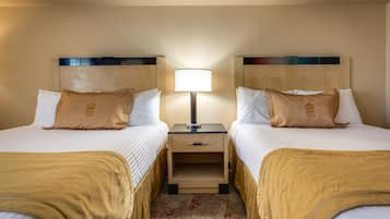 Une chambre d’hôtel avec deux lits, chacun doté d’une tête de lit marron, d’une table de chevet avec une lampe et d’un petit tiroir.