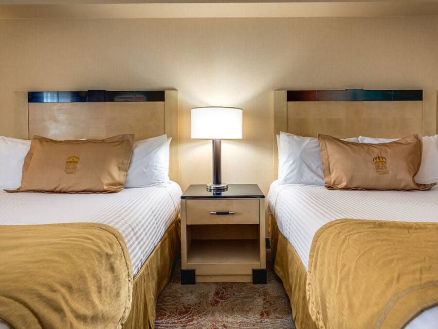 Une chambre d’hôtel avec deux lits, chacun doté d’une tête de lit marron, d’une table de chevet avec une lampe et d’un petit tiroir.