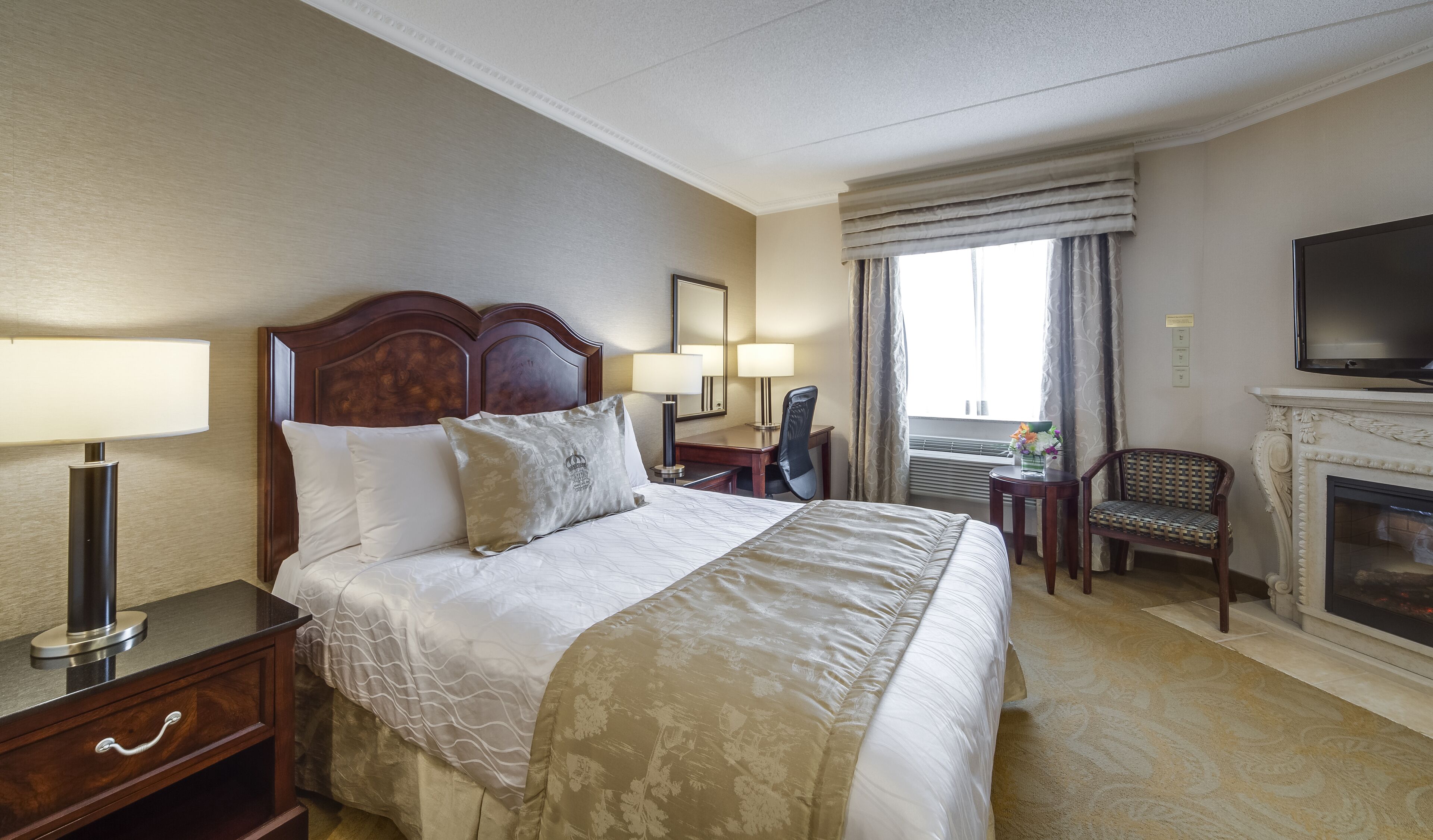 Een hotelkamer met een groot bed, een bureau, een stoel, een televisie en een open haard.