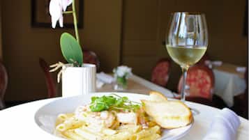 A plate of pasta with shrimp and bread, a glass of white wine, and a vase with flowers on a table.
