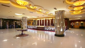 A spacious lobby with a modern design, featuring a reception desk, decorative lighting, and a polished floor.