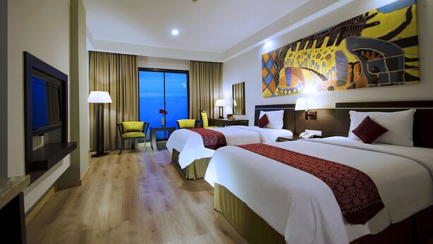 A hotel room with two beds, a TV, a desk, and a large window with a view.