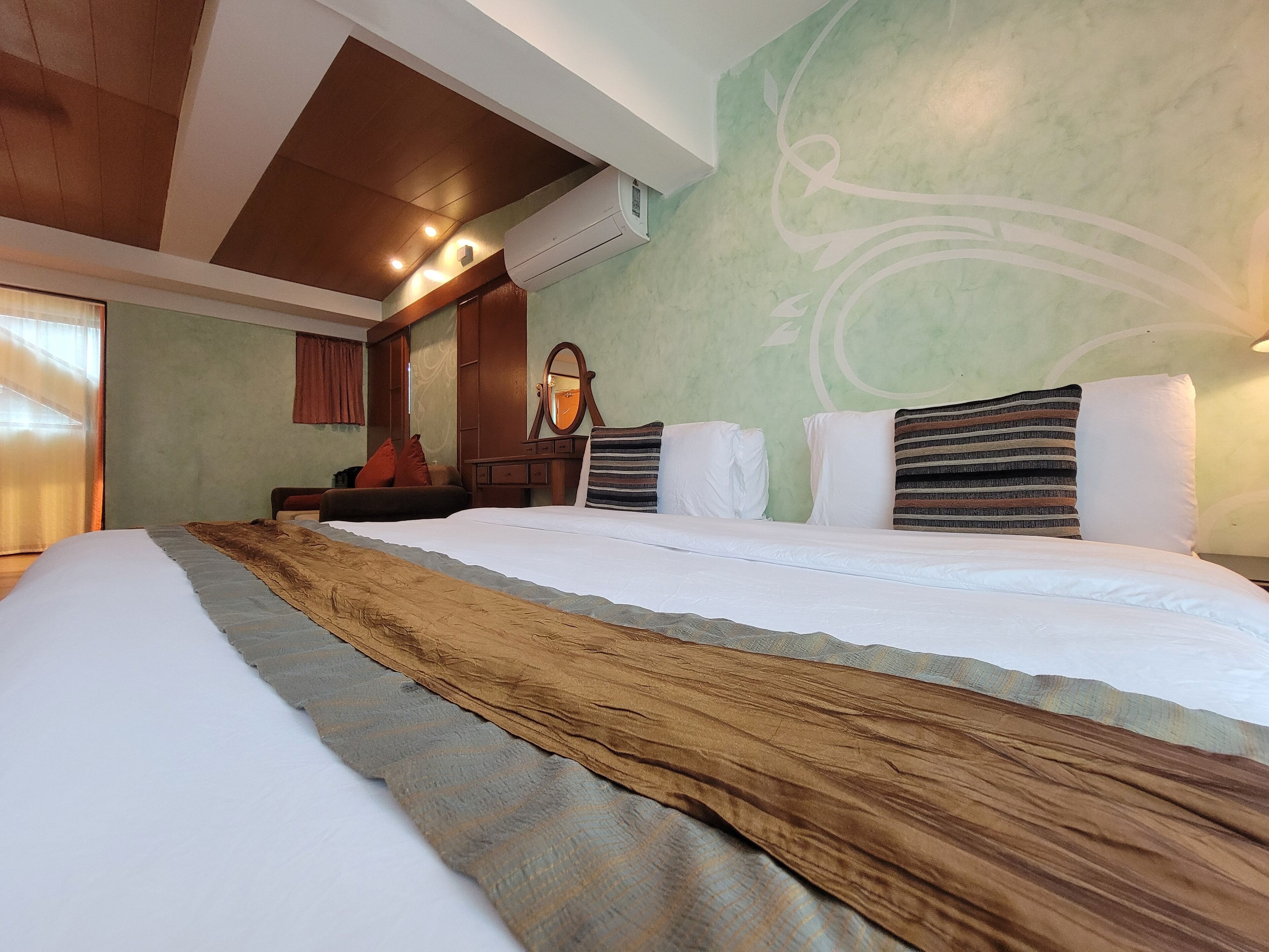 A hotel room with a large bed, a wooden headboard, a mirror, and a green wall with a decorative design.
