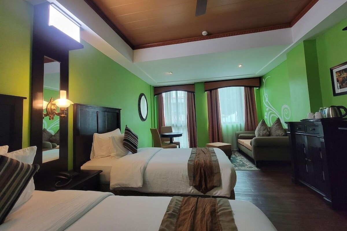 Habitación de hotel con dos camas, un escritorio, una silla, un sofá, un armario y un ventilador de techo.