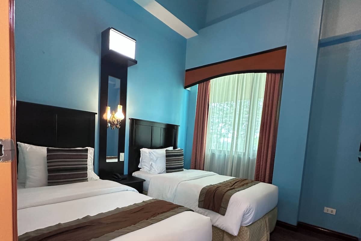 A hotel room with two beds, a nightstand, a mirror, and a window with curtains.