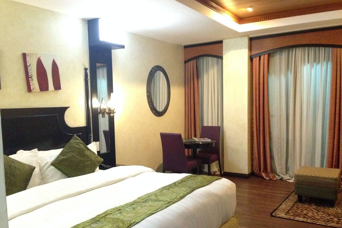 A hotel room with a bed, a desk, a chair, a mirror, and a window with curtains.