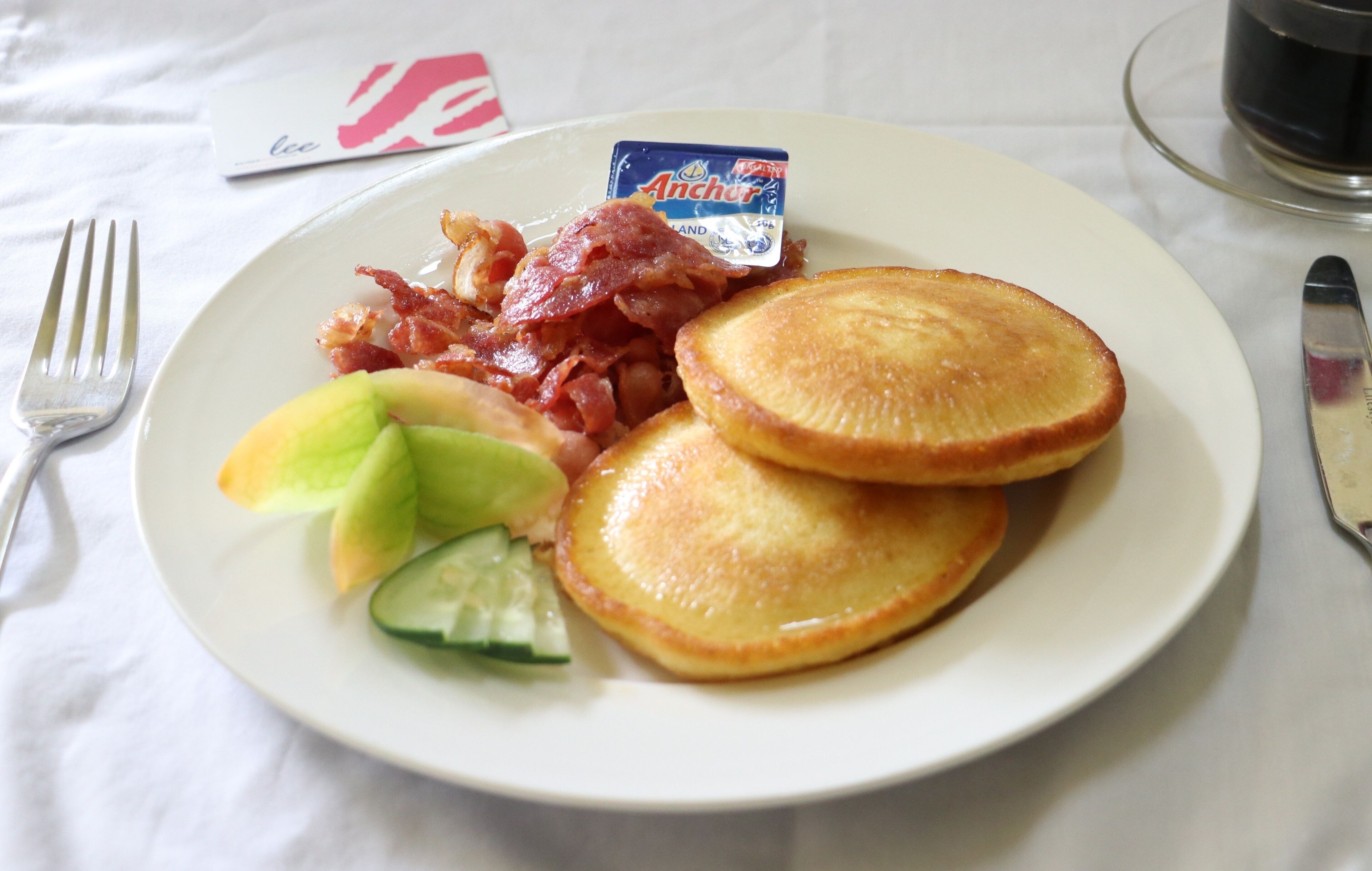 Ein Teller mit Pfannkuchen, Speck und Obst auf einer weißen Tischdecke.