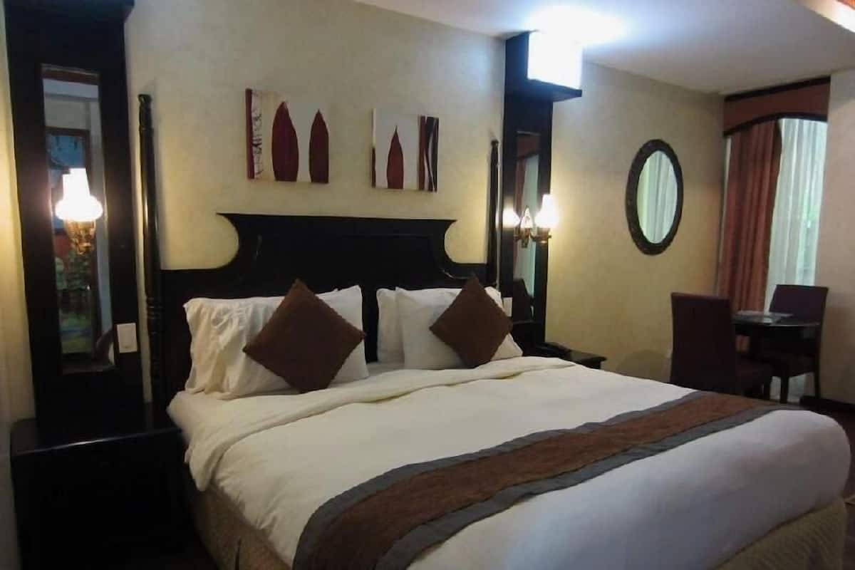 A hotel room with a large bed, a nightstand, a desk, and a chair.