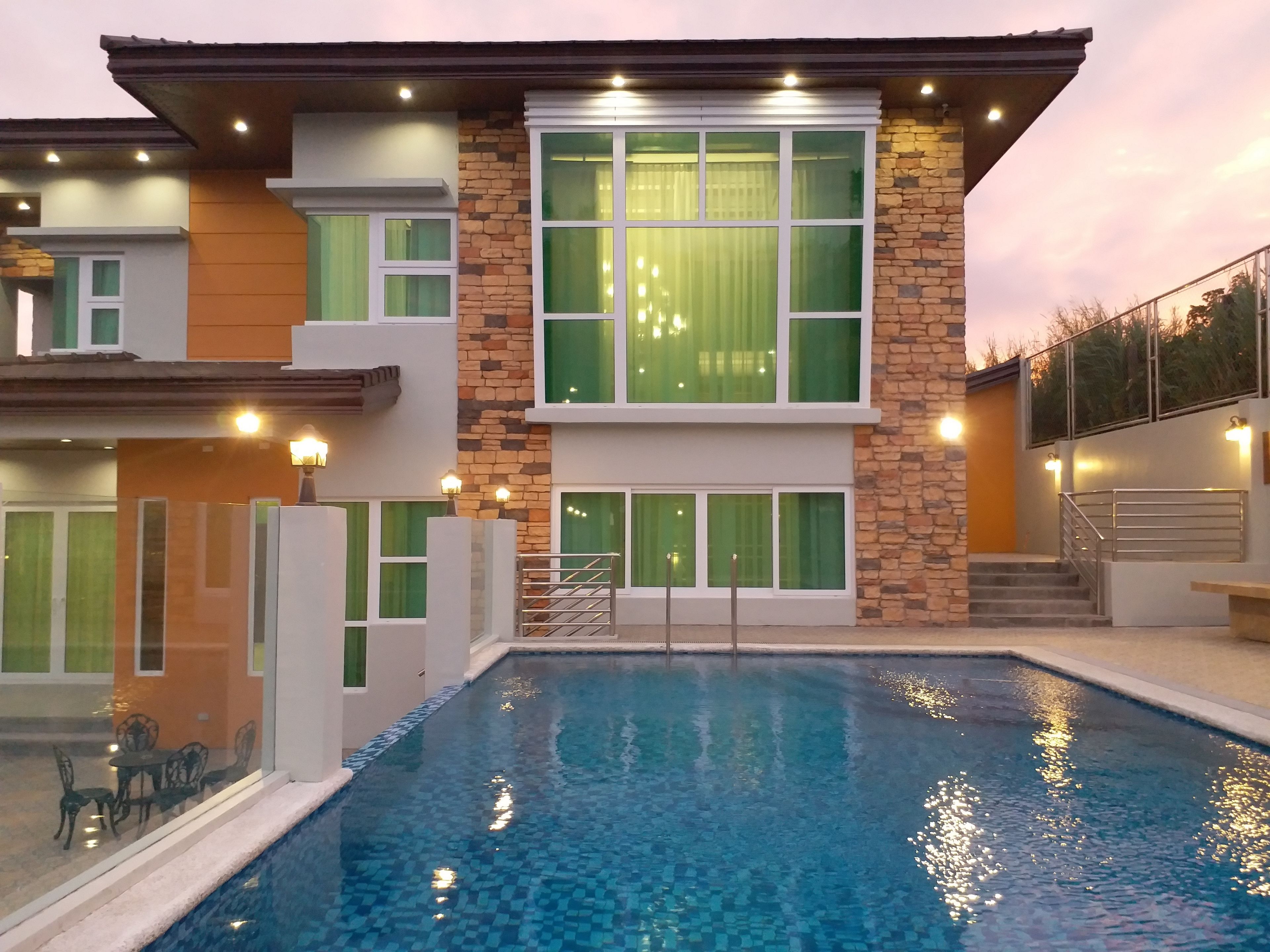 A modern two-story house with a swimming pool, large windows, and outdoor lighting.