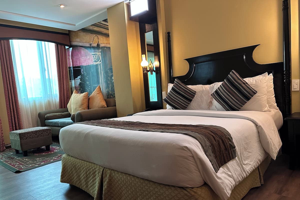 A hotel room with a large bed, a sofa, a small table, and a window with curtains.