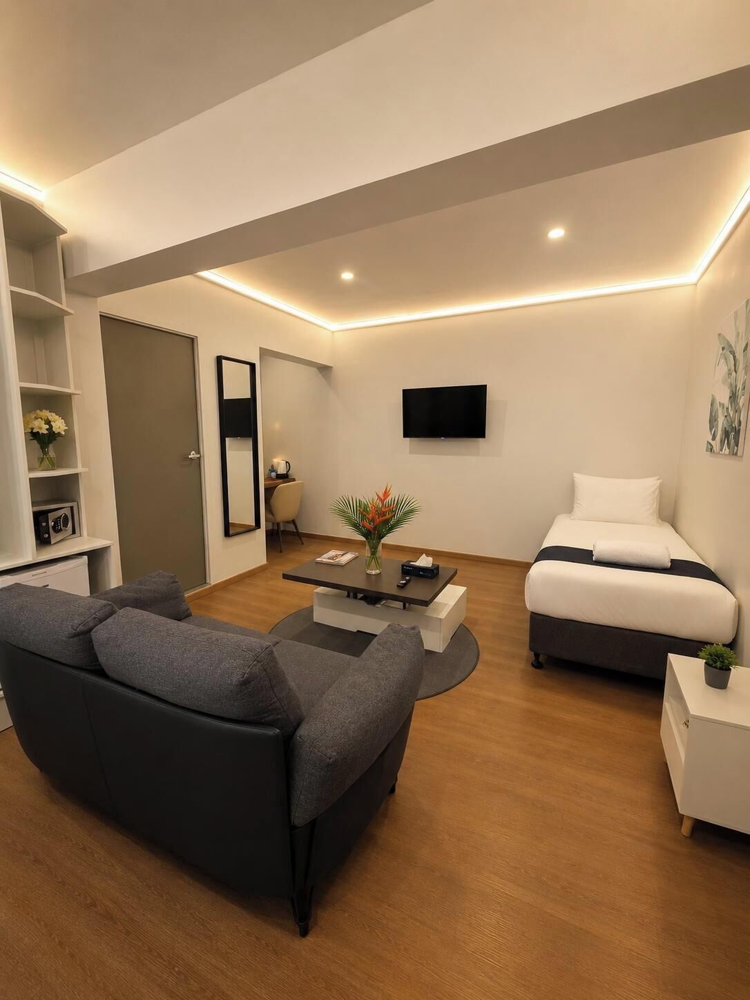 A modern living room with a sofa, a coffee table, a TV, and a bed.