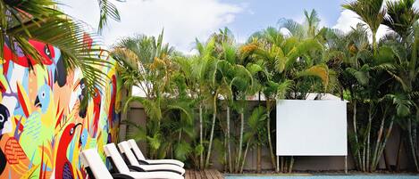 Zona de piscina con sillones de descanso y un mural colorido.