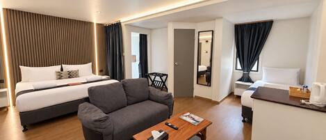 A modern hotel room with a bed, sofa, desk, and a small table with a remote control and tissues.