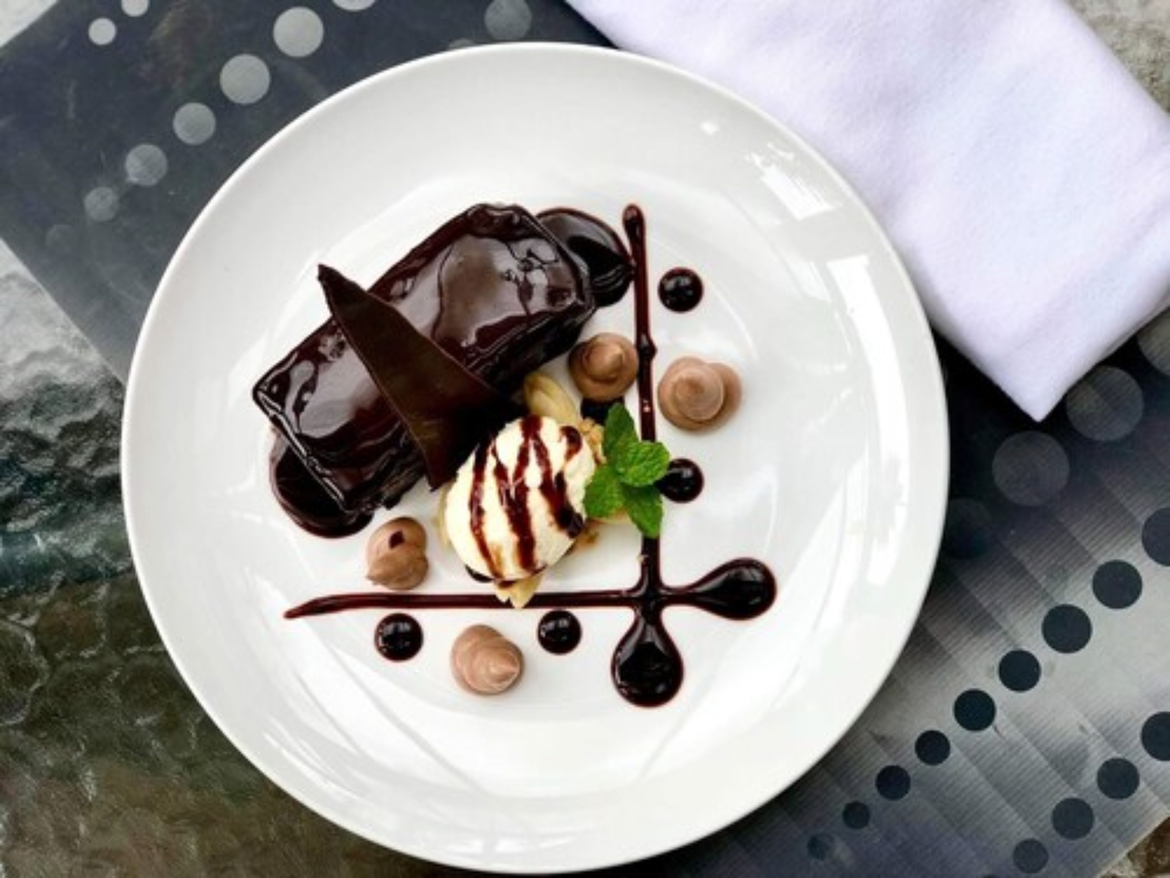 Un plato de postre con preparaciones cubiertas de chocolate y una bola de helado, decorado con hojas de menta.