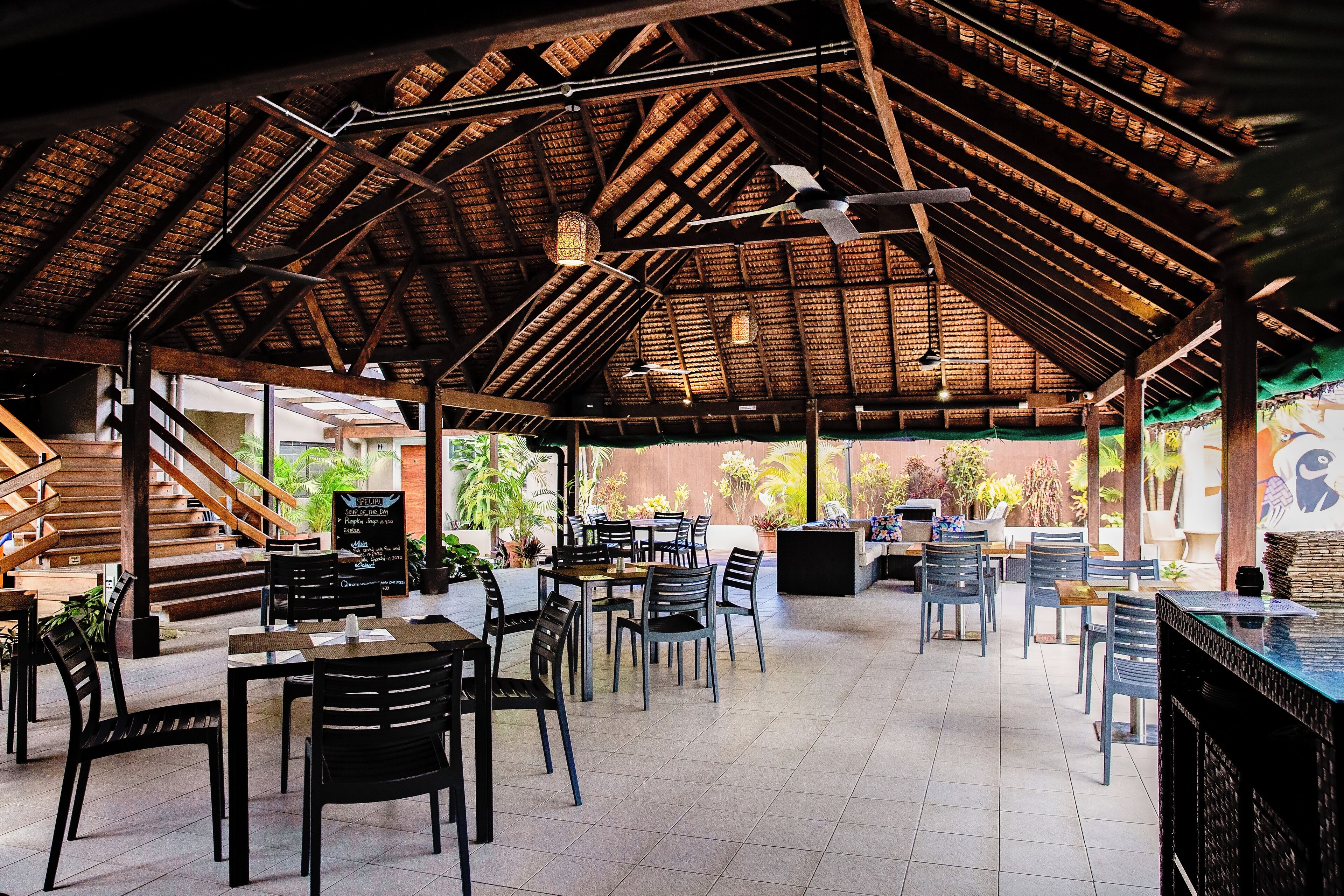 An indoor dining area with wooden beams, tables, chairs, and a staircase.
