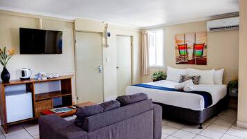 A hotel room with a bed, a sofa, a TV, a desk with a computer, and a window with curtains.