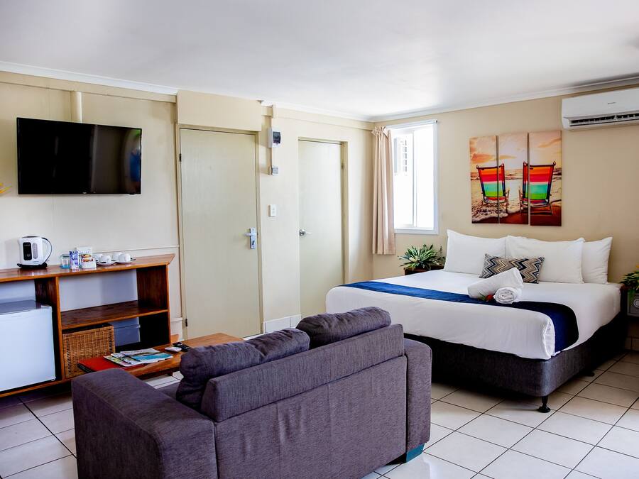 A hotel room with a bed, a sofa, a TV, a desk with a computer, and a window with curtains.